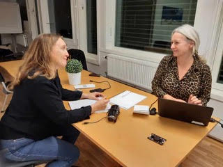 Heidi and Anne sitting at a table with a notepad and a computer